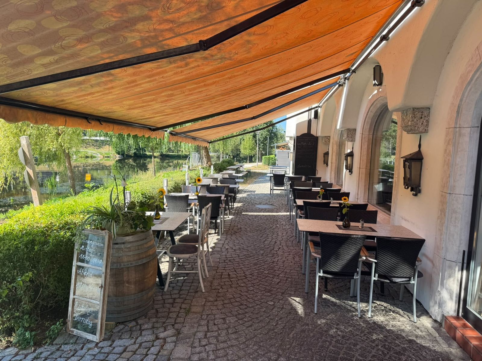 Terrasse entlang des Hauses mit gedeckten Tischen, Sonnenblumen und Flussblick
